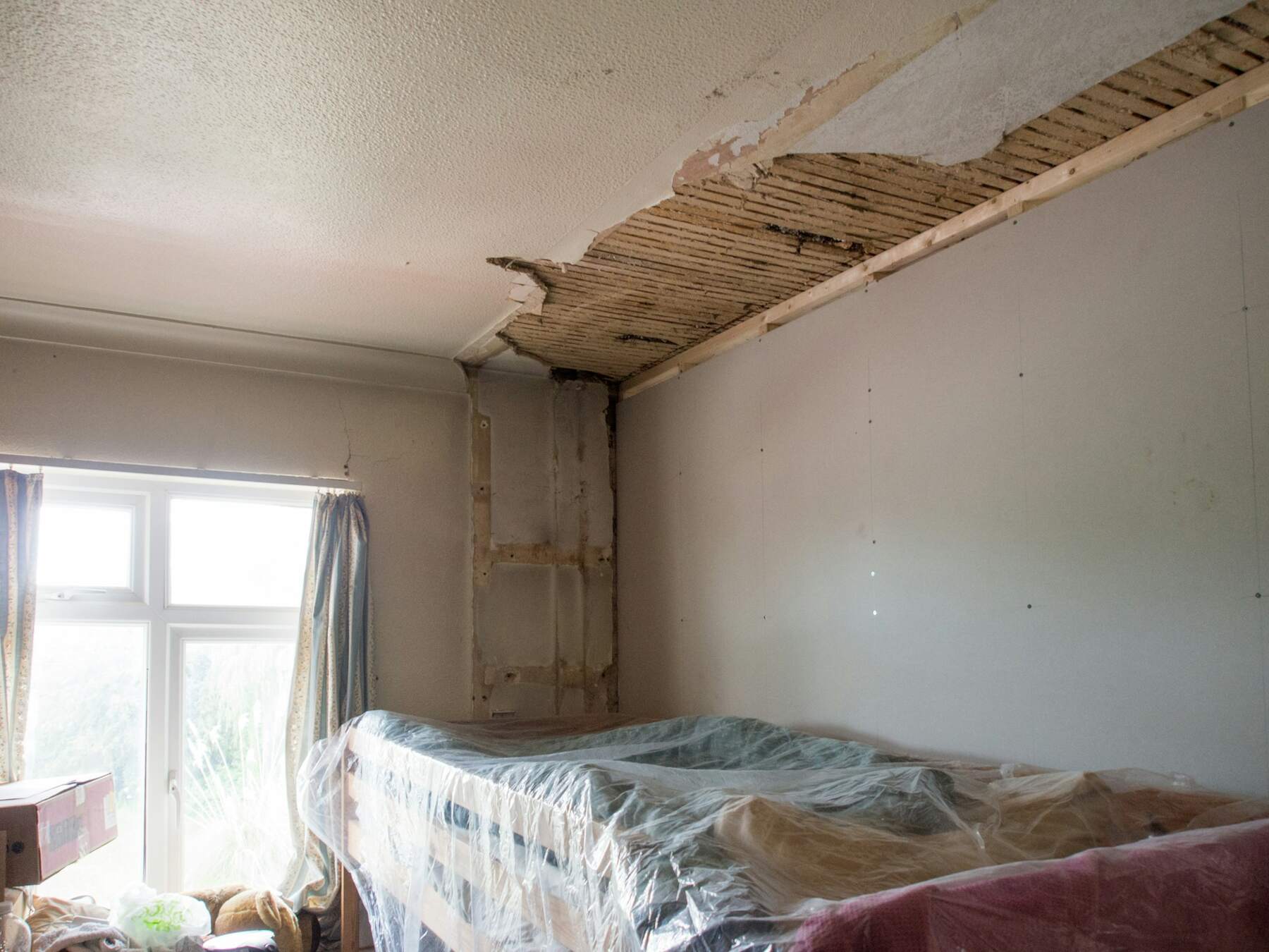 Bedroom under renovation with exposed ceiling and plastic-covered bed