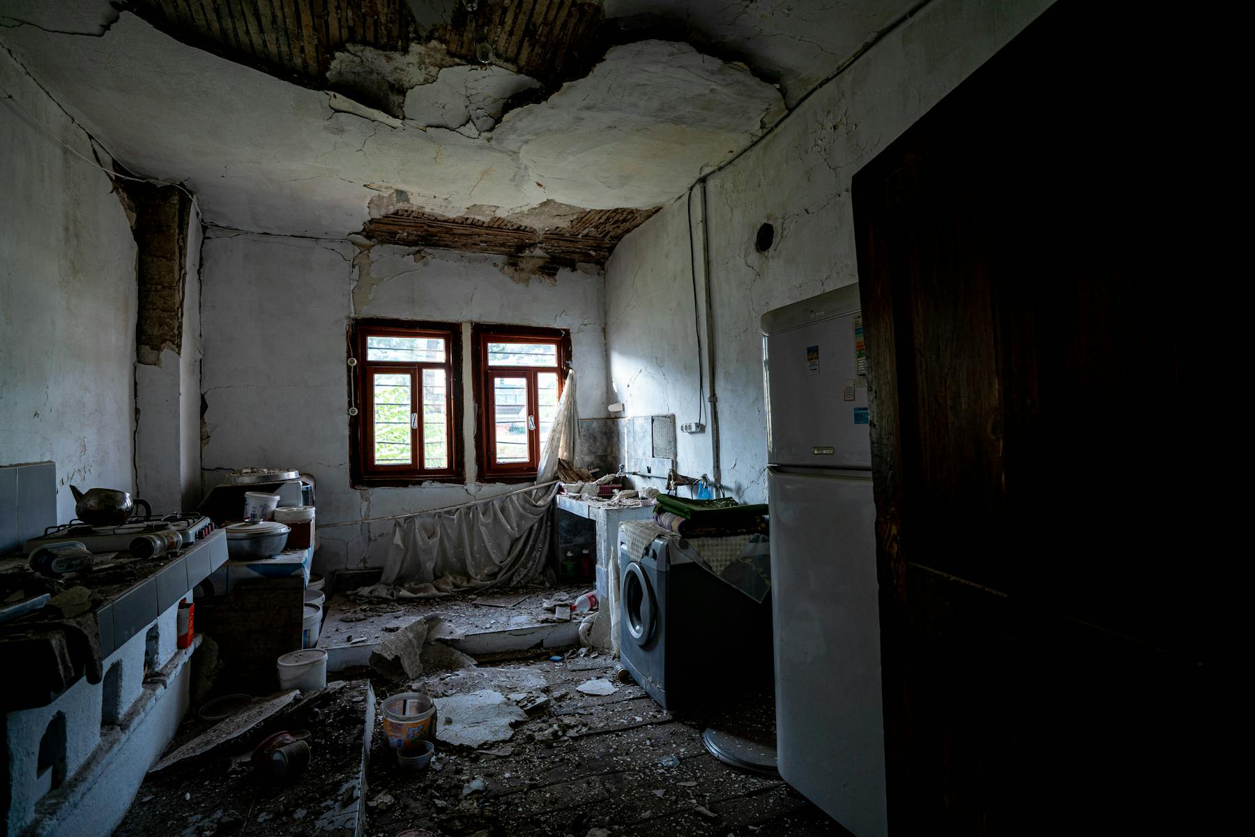 Old, damaged kitchen with cracked ceiling and debris on the floor