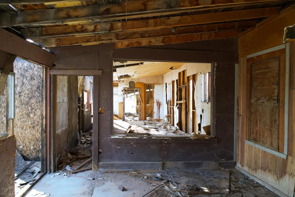 Abandoned house interior with exposed beams, broken walls, and scattered debris