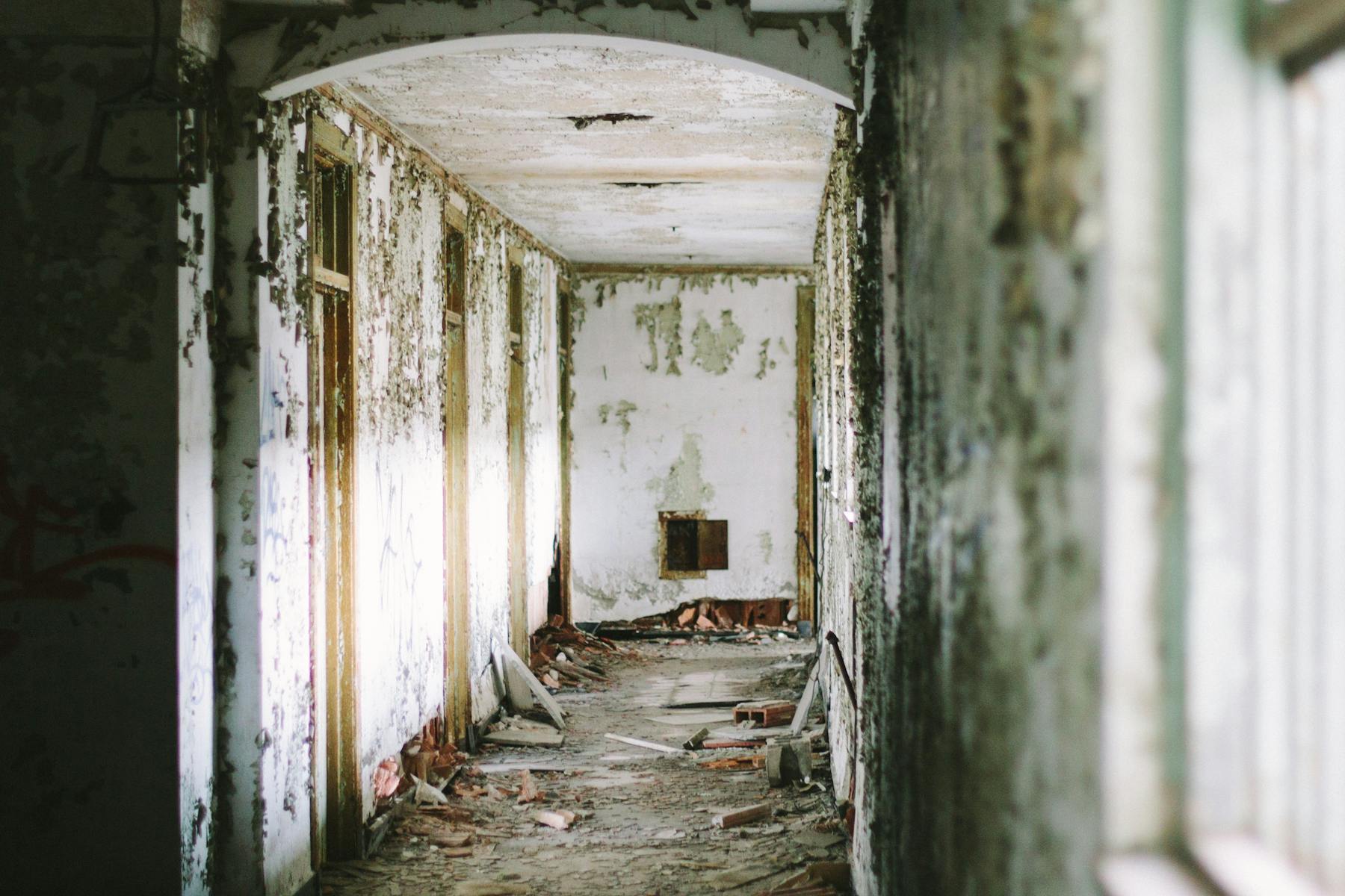 Decaying hallway with peeling paint and debris on the floor