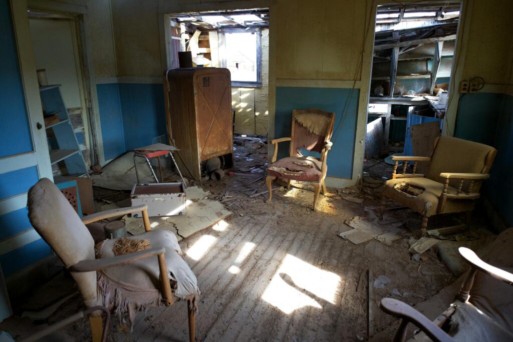 Abandoned room with old chairs, debris, and sunlight on the floor