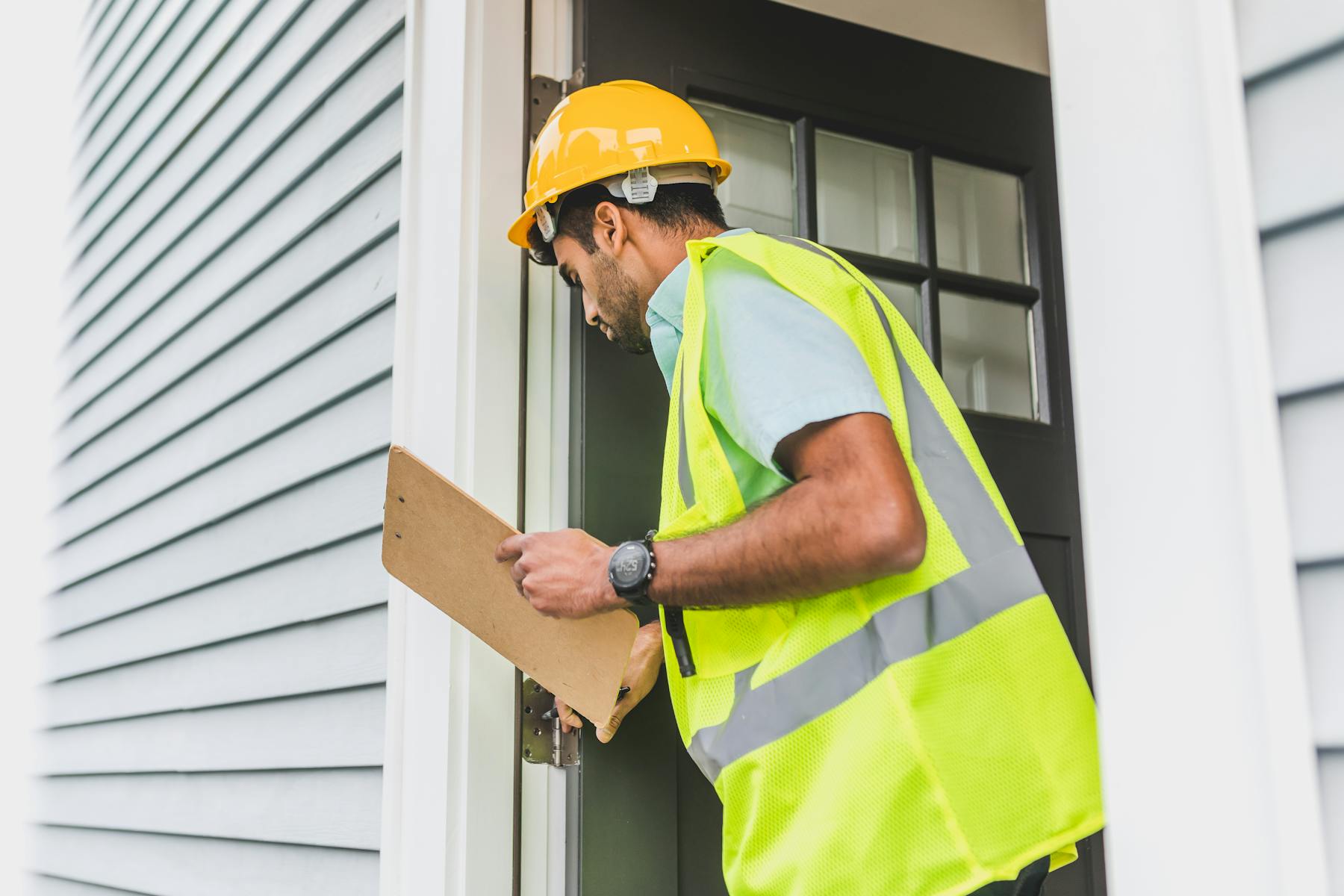 Worker inspecting home exterior with clipboard