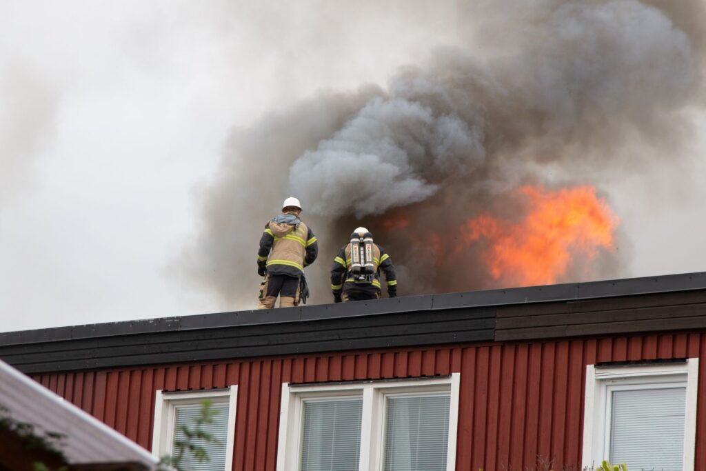 Firefighters on roof near flames and heavy smoke