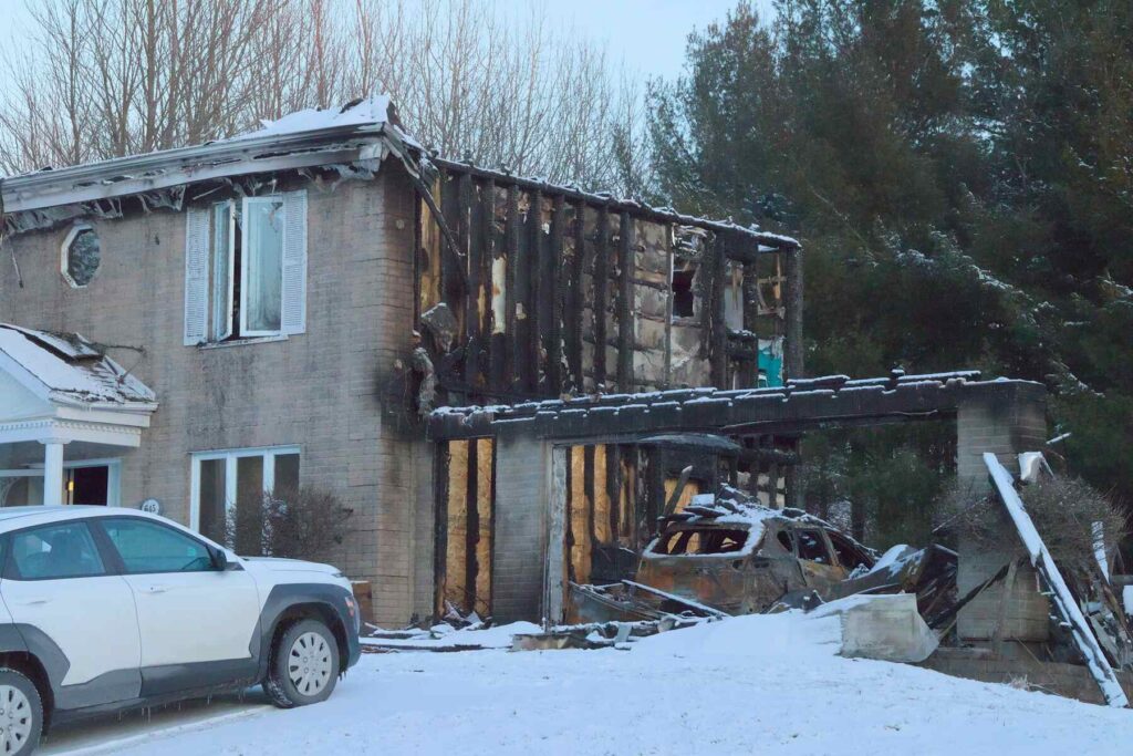 Fire-damaged home exterior with burned walls and snow