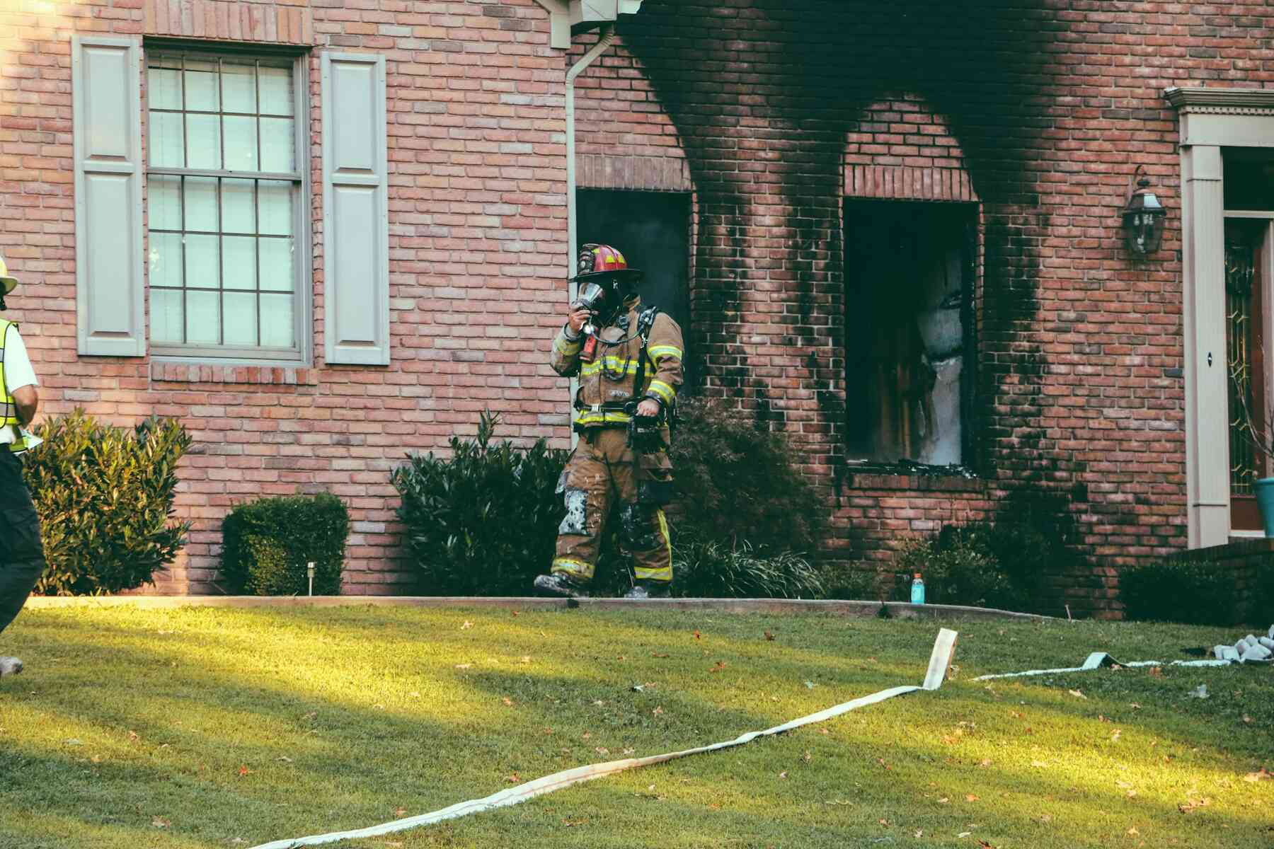 Firefighter outside brick home with smoke damage