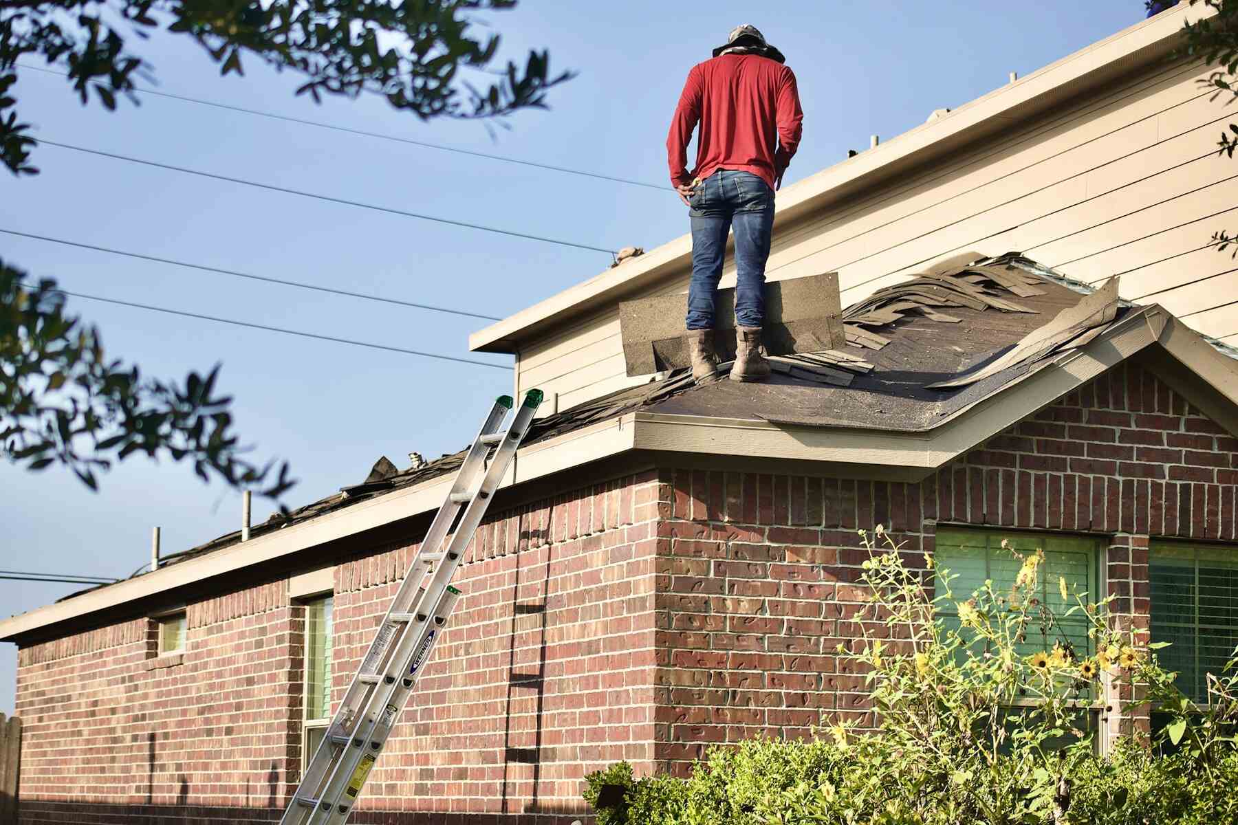 Roofer removing old shingles from a residential roof during replacement