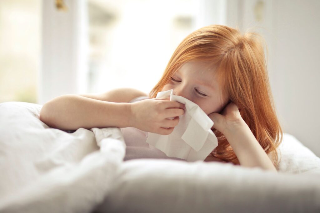 Child resting in bed and blowing her nose with a tissue