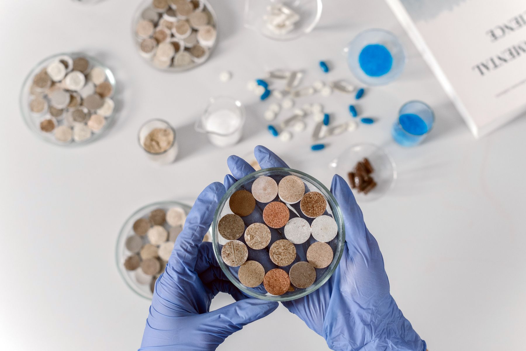 Gloved hands examining material samples in a laboratory dish