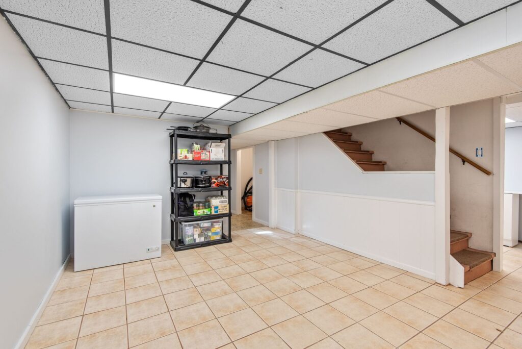 Basement storage area with tile flooring, shelving, and stairs