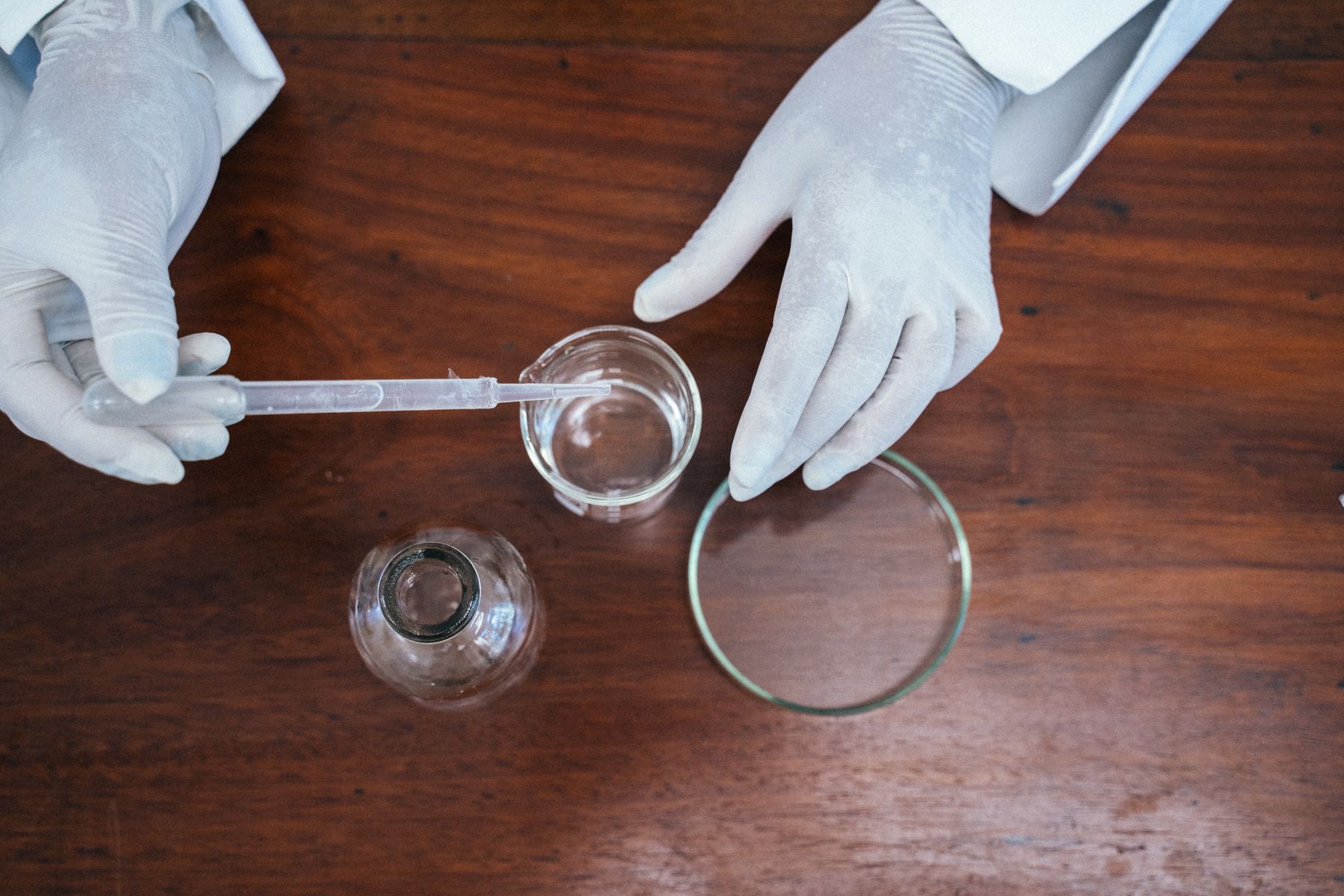 Gloved hands using a dropper with laboratory glassware