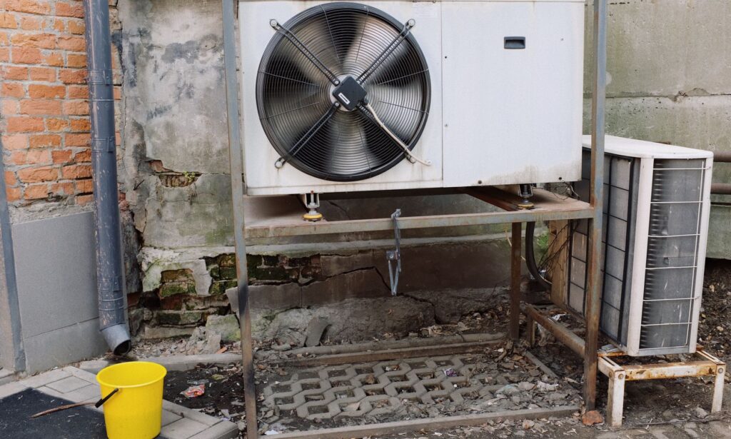 Outdoor air conditioning units mounted beside a weathered brick and concrete wall