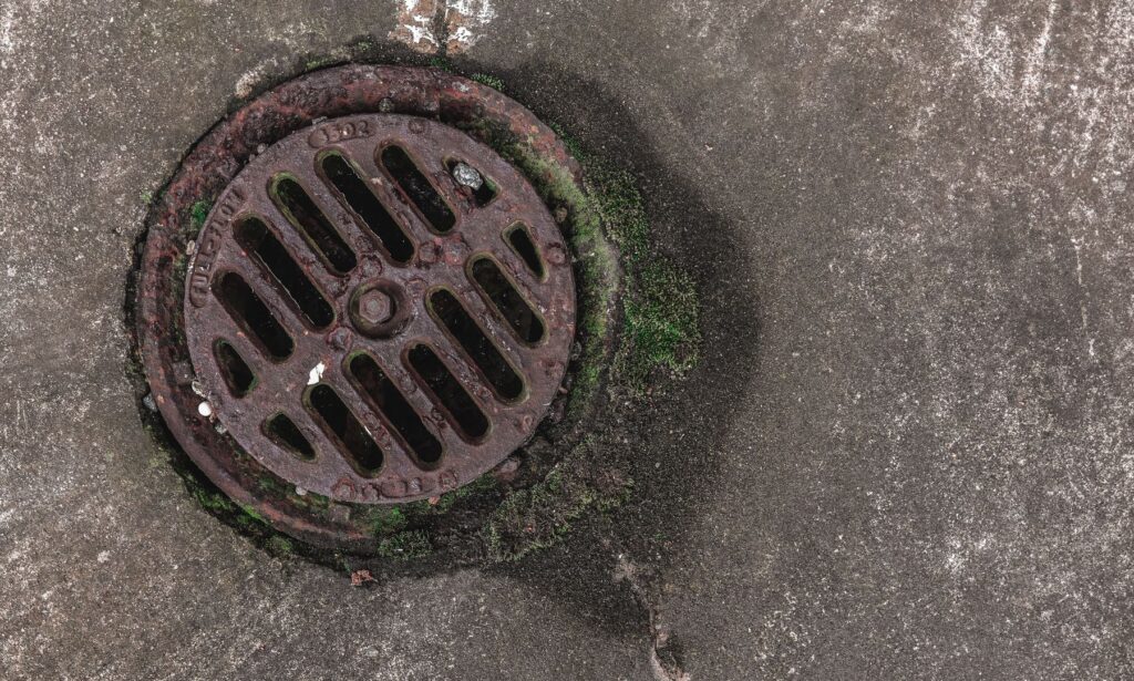 Rusty circular drain grate surrounded by moss on a weathered concrete surface