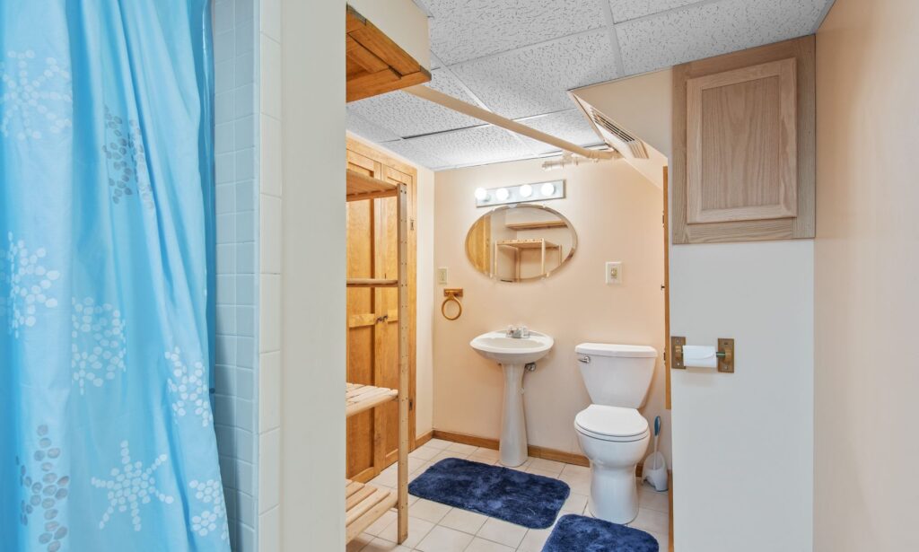 Bathroom with a blue shower curtain, white sink, toilet, wooden shelves, and tiled floor