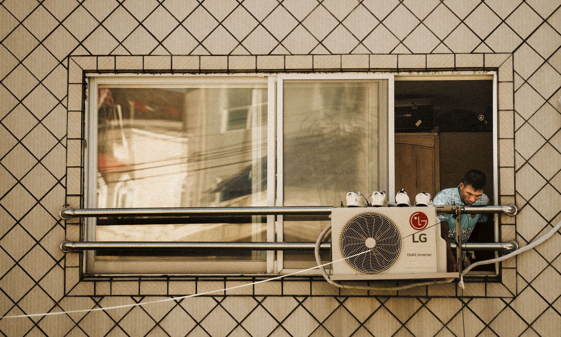 Man leaning out of a window beside an outdoor air conditioning unit mounted on a tiled building