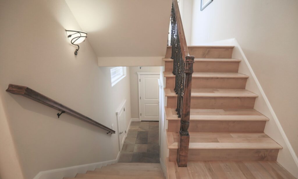 Wooden staircase with dark railings, beige walls, and a window overlooking a lower landing