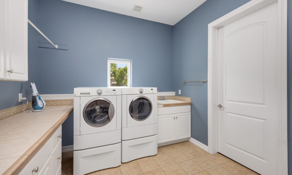 Laundry room with blue walls, white washer and dryer, utility sink, and tiled flooring
